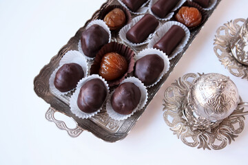 Traditional Turkish Candied Chestnuts in silver tray with chocolate - covered chestnut candy on white surface with coffee cup