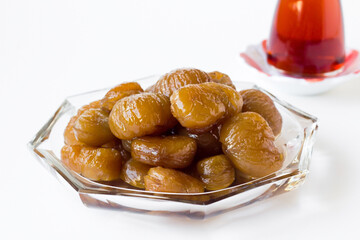 Traditional Turkish Candied Chestnuts designed in glass plate on white surface with tea