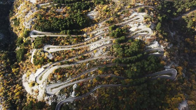 A car winds along a serpentine road through a breathtaking mountain landscape, captured from above. The aerial view reveals mountains draped in rich green moss, highlighting the serene power and