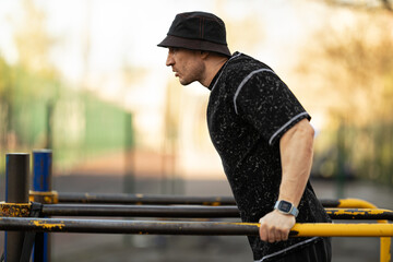 man is engaged in fitness training park using parallel bars perform dips. setting features sunny...