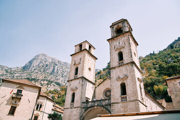 Fototapeta premium Bell towers of the Cathedral of St. Tryphon among ancient houses at the foot of the mountains. Kotor, Montenegro