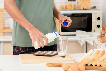 Close up hands of active strong man pouring fresh pure milk into glass in morning, male drink milk in cup after wake up for health and wellbeing in kitchen in house. Healthy lifestyle concept.