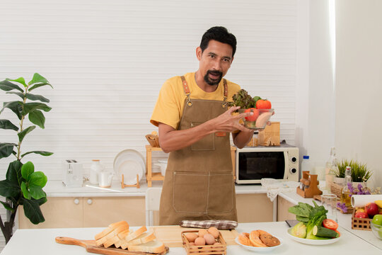 Asian bearded man introducing ingredients and cooking process communicating with subscribers through camera while streaming live on social media. A male blogger share cooking steps.