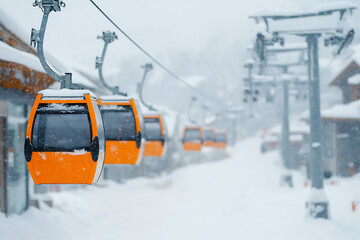 Orange gondolas ascend through falling snow, their vibrant color contrasting with the muted winter landscape. A scenic mountain adventure.