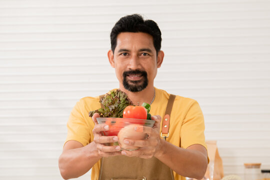 Asian bearded man introducing ingredients and cooking process communicating with subscribers through camera while streaming live on social media. A male blogger share cooking steps.