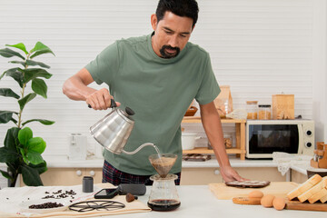 Indian or Hispanic man with beard and mustache prepares pouring-over coffee with hot water carefully in cup in kitchen routine morning activity, coffee before start work in workplace at home office