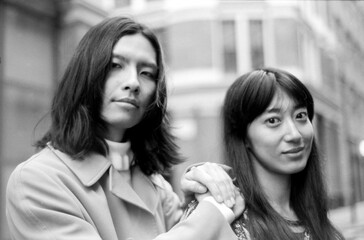 Young couple holding hands, wearing coats in urban setting, grainy monochrome film aesthetic