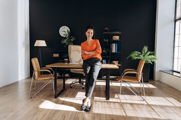 Confident businesswoman leaning on desk in modern office