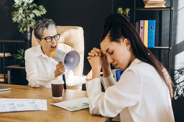 Angry senior manager shouting at employee through megaphone in office