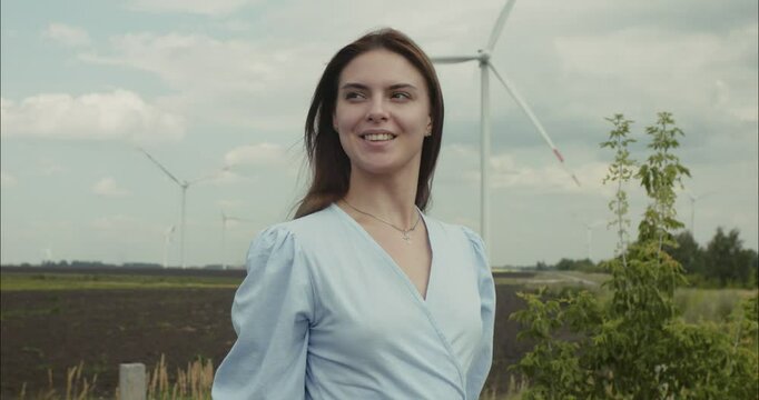Young woman smiling near wind turbines in agricultural field