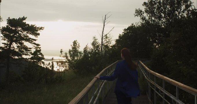 Woman walking on wooden path at sunset near the sea