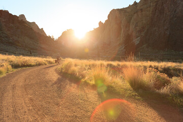 Wilderness road leading towards a rocky craig with sunburst over the peaks