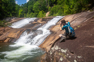 Hiker with backpack taking photos of a waterfall in a scenic location