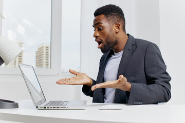 Stressed businessman in formal attire holding head in frustration while working on laptop at office...
