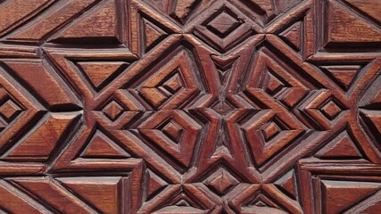 Close up of ornate, carved wooden door surface with geometric patterns, dark wood texture with starburst shapes, rich details and traditional craftsmanship.
