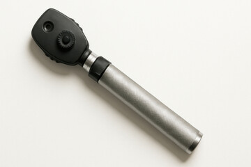 Handheld medical ophthalmoscope with metallic handle and black head, used for eye examinations on white background