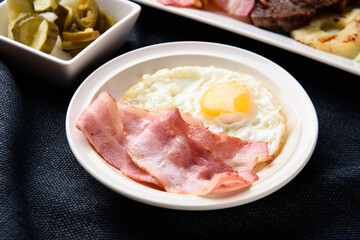 Baked bacon and fried eggs on a white plate
