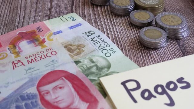 Primer plano de un escritorio con una nota adhesiva que contiene un mensaje que dice pagos y billetes de 200 y 100 pesos cerca de monedas afiladas y una calculadora.