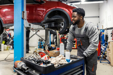 Interracial hardworking smiling car service worker pushing toolbox around workshop and preparing...