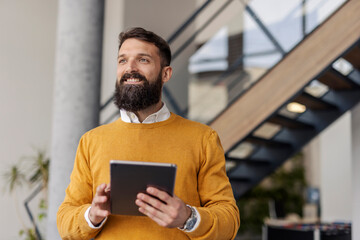 Portrait of happy executive standing at corporate office with tablet in hands and looking away.