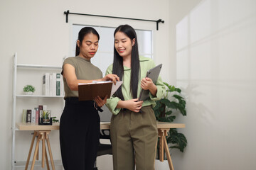 Portrait of Two Asian business woman standing in an office, holding documents and discussing work. Business ideas and strategies