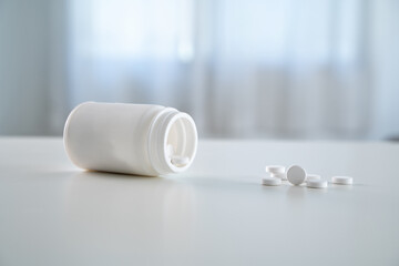 A white pill bottle with pills on a table. The pills are white and small in size. The table is clean