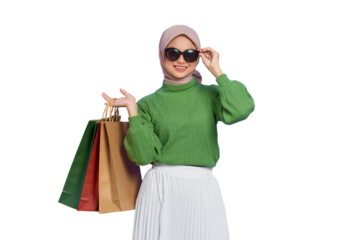 Cheerful beautiful Asian woman in green sweater and sunglasses holding shopping bags isolated on transparent background