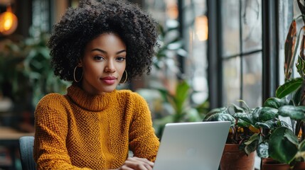 Smiling young African American woman working on laptop computer in cozy modern coffee shop or coworking space environment  Freelance startup small business remote work and productivity concept