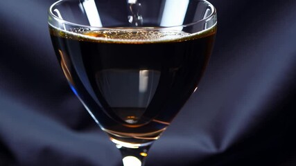 Close-up 360-degree rotation video of a coupe glass with a splash of liquid, side-lit on dark velvet - Powered by Adobe