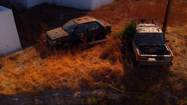 Two old, rusty, abandoned cars missing parts in Milos, Greece. Sunset light adds a nostalgic and moody atmosphere to the scene.