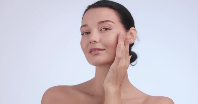 Confident barefaced woman caresses her cheek with a healthy glow, perfect for beauty brand campaigns, skincare product launches, and cosmetics promotional material for flawless skin.