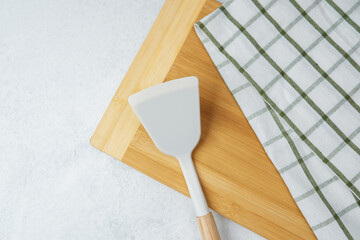 Wooden chopping board with a spatula and kitchen towel on a white background