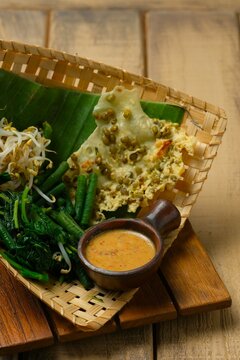 Pecel pincuk or Pecel Madiun on brown background. Traditional food from Indonesia and Malaysia. Vegetables salad with peanut sauce, served with mungbean cracker.