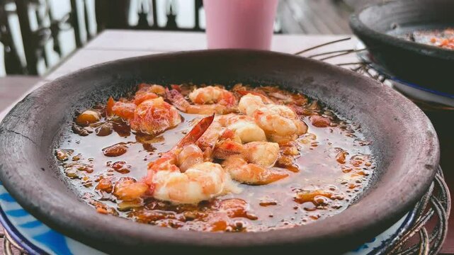 Pan-seared shrimp in spicy sambal served sizzling hot in a traditional clay mortar. Indonesian seafood dish called Gammi Udang
