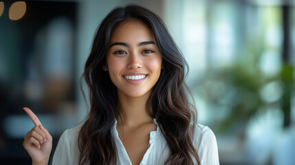 Fototapeta premium 指を上に向ける女性オフィスで笑顔を見せる若い女性のポートレート
