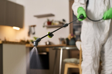 Close-up of worker in suit spraying in the room and disinfecting apartment from insects