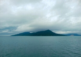 Scenic view of a tropical island surrounded by calm ocean under a cloudy sky, perfect for travel, nature, and landscape themes in editorial and commercial use.