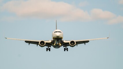 Aircraft approaches runway under clear skies with distant clouds during sunny day