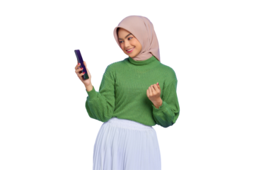Excited beautiful Asian woman in green sweater and hijab using a mobile phone, celebrating success, getting good news isolated on transparent background