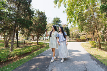 Fototapeta premium Two Friends Strolling Along a Sunlit Path in a Lush Green Park, Capturing Memories and Enjoying Nature's Beauty Together