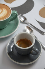 a small cup of espresso with cappuccino coffee behind