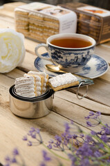 A cup of tea, a white flower, and a stack of cookies sit on a wooden table.