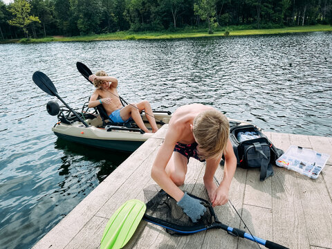 Preteen boys on dock and kayak fishing from lakeside dock