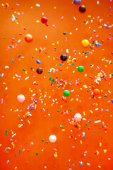 Candy sprinkles scattered against orange background vertical