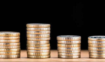 Stacks of shiny coins arranged in ascending order on a wooden surface with a black background illustrating the concept of wealth and financial growth
