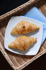 two croissants on a white plate in  woven basket
