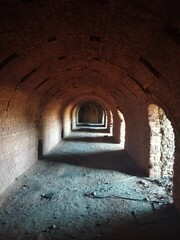 Obraz premium Tunnel interior with light at the end, photo of an old red brick arched tunnel with side passages flooded with sunlight.