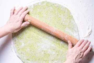 Women's hands roll out green dough with spinach with a rolling pin. The concept of healthy eating. Top view.