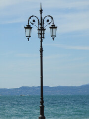 Eine Laterne vor dem blauen Wasser des Gardasees bei Lazise