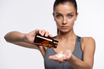 Closeup of fitness woman holding bottle with vitamins, capsules or pills and standing isolated